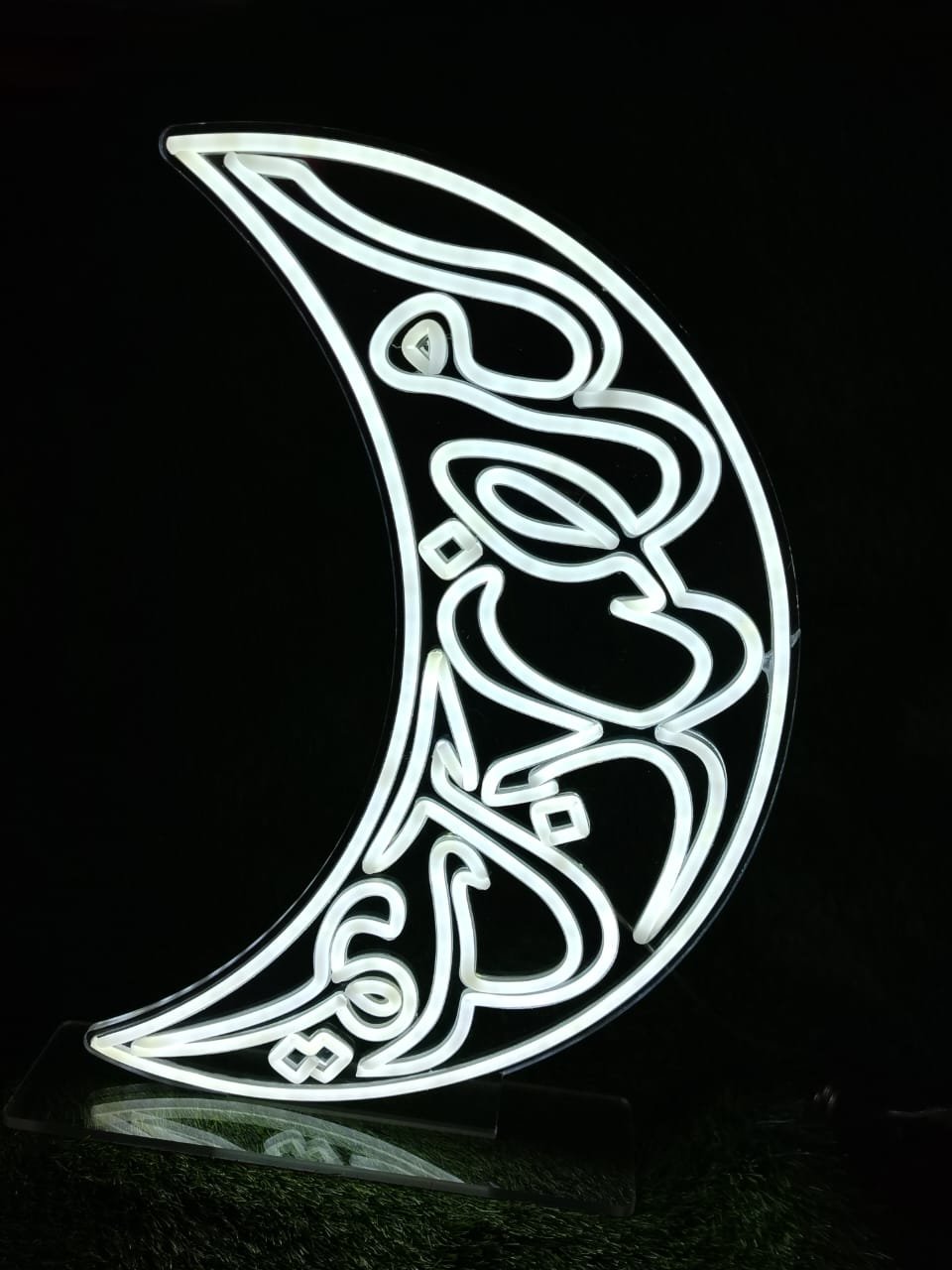 White neon light frame shaped like a crescent moon with "Ramzan Kareem"